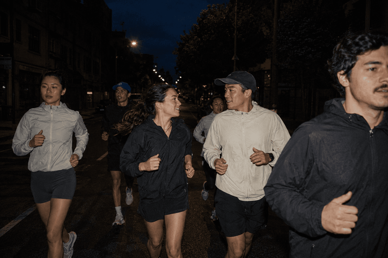A group running together through city streets at night, mid-conversation.